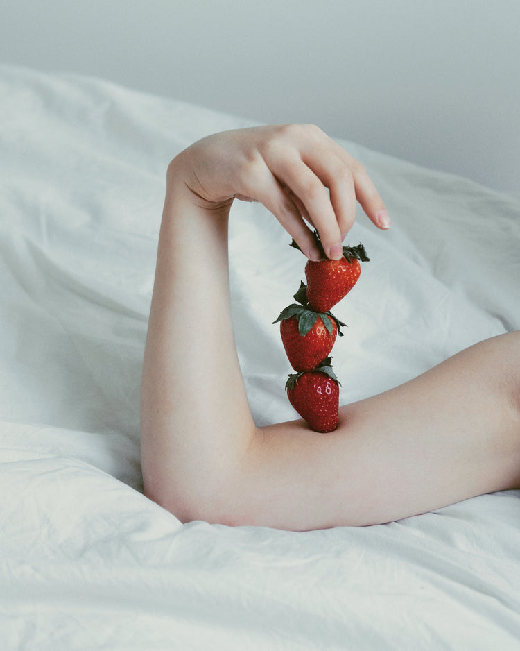 Female arm resting on a sheet with three strawberries stacked on her skin.