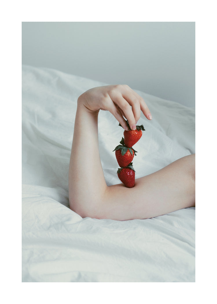 Female arm resting on a sheet with three strawberries stacked on her skin.