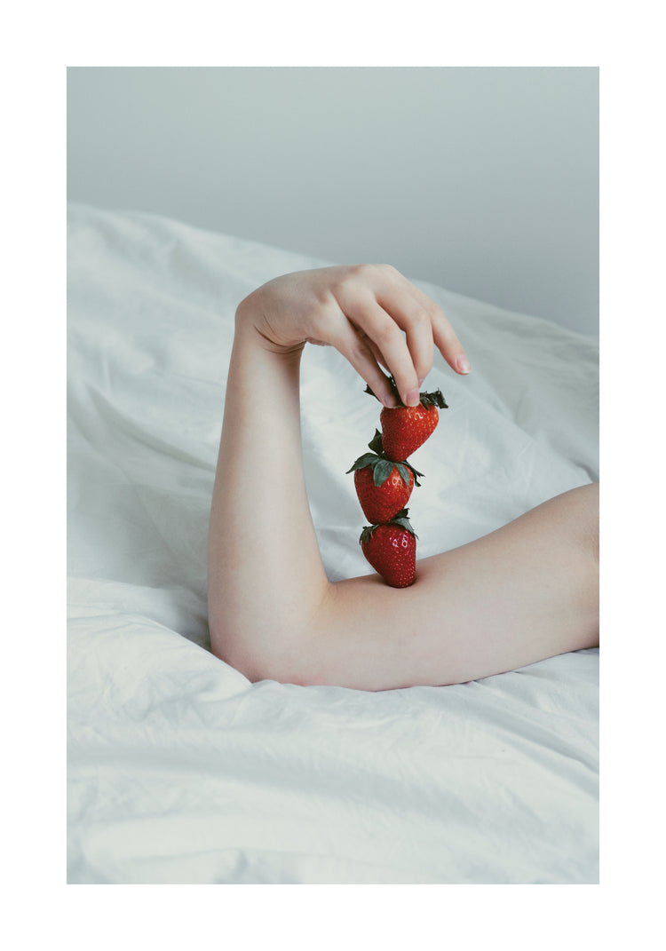 Female arm resting on a sheet with three strawberries stacked on her skin.
