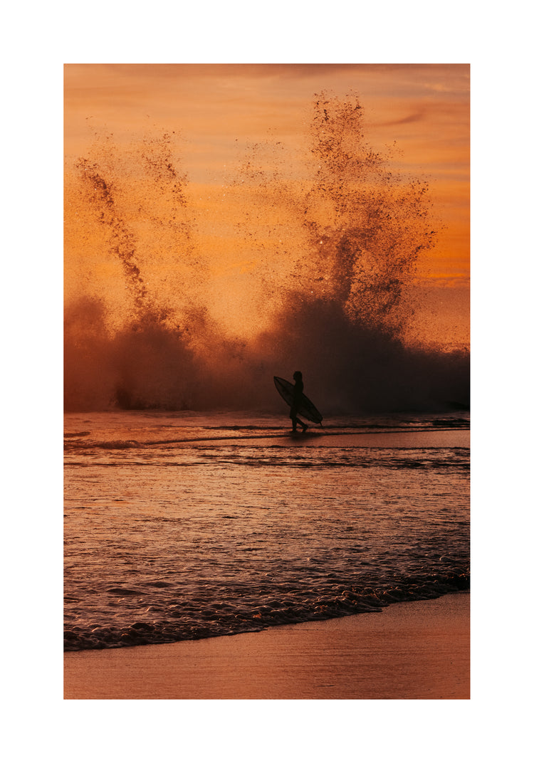 Surfer heading out into the orange waves during sunset.