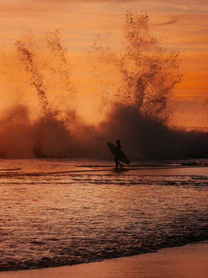 Surfer heading out into the orange waves during sunset.
