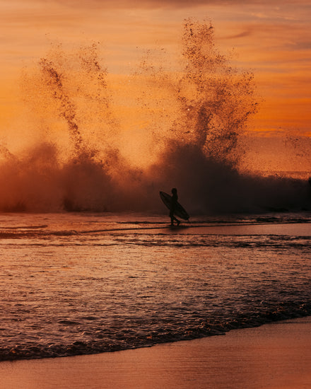 Surfer heading out into the orange waves during sunset.