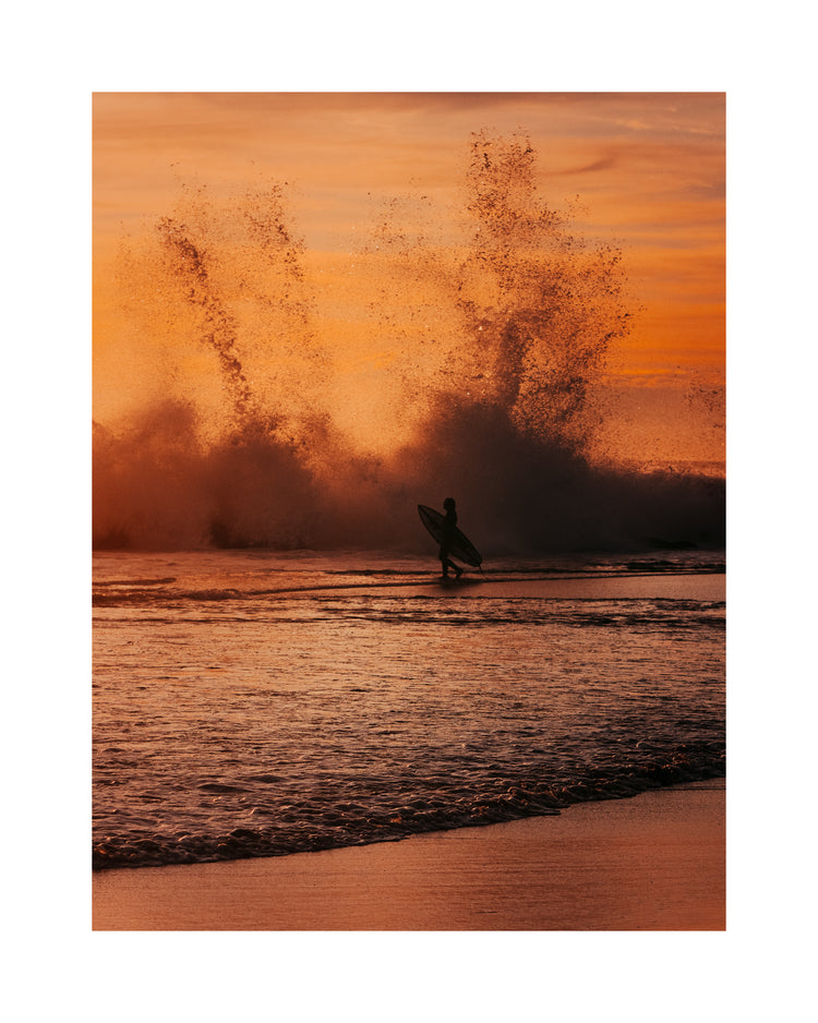 Surfer heading out into the orange waves during sunset.