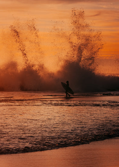Surfer heading out into the orange waves during sunset.