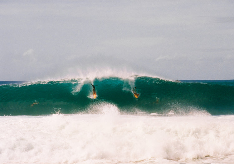 Two surfers photographed as they are taking off the same wave