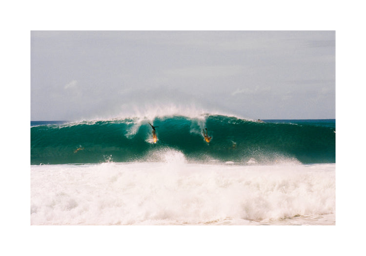 Two surfers photographed as they are taking off the same wave
