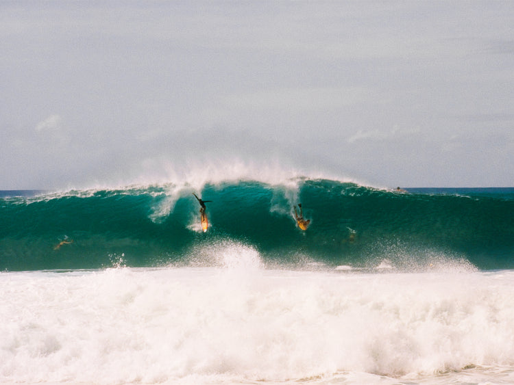 Two surfers photographed as they are taking off the same wave