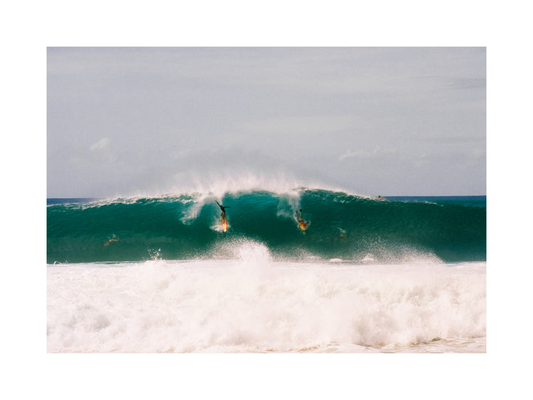 Two surfers photographed as they are taking off the same wave