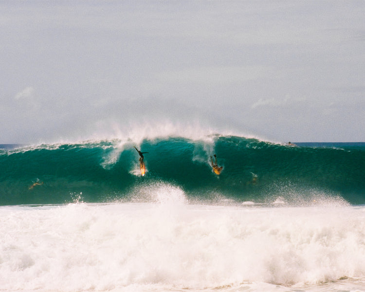 Two surfers photographed as they are taking off the same wave