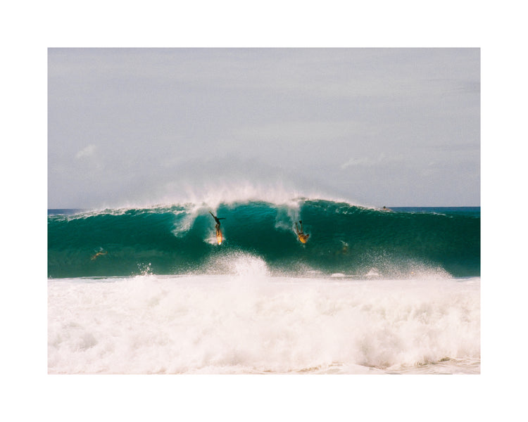 Two surfers photographed as they are taking off the same wave