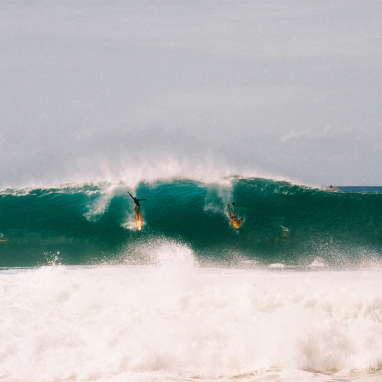 Two surfers photographed as they are taking off the same wave