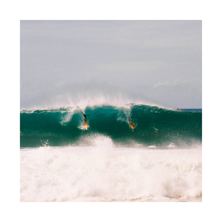 Two surfers photographed as they are taking off the same wave