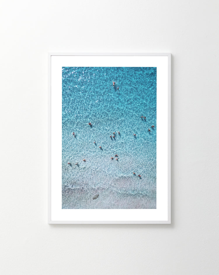 The Eavesdropping VIII Poster captures a beach scene with clear turquoise water, resembling a perfect Tinder match. Tiny figures swim and play, creating ripples as the sand shifts from light to dark beige from shore to deeper waters.