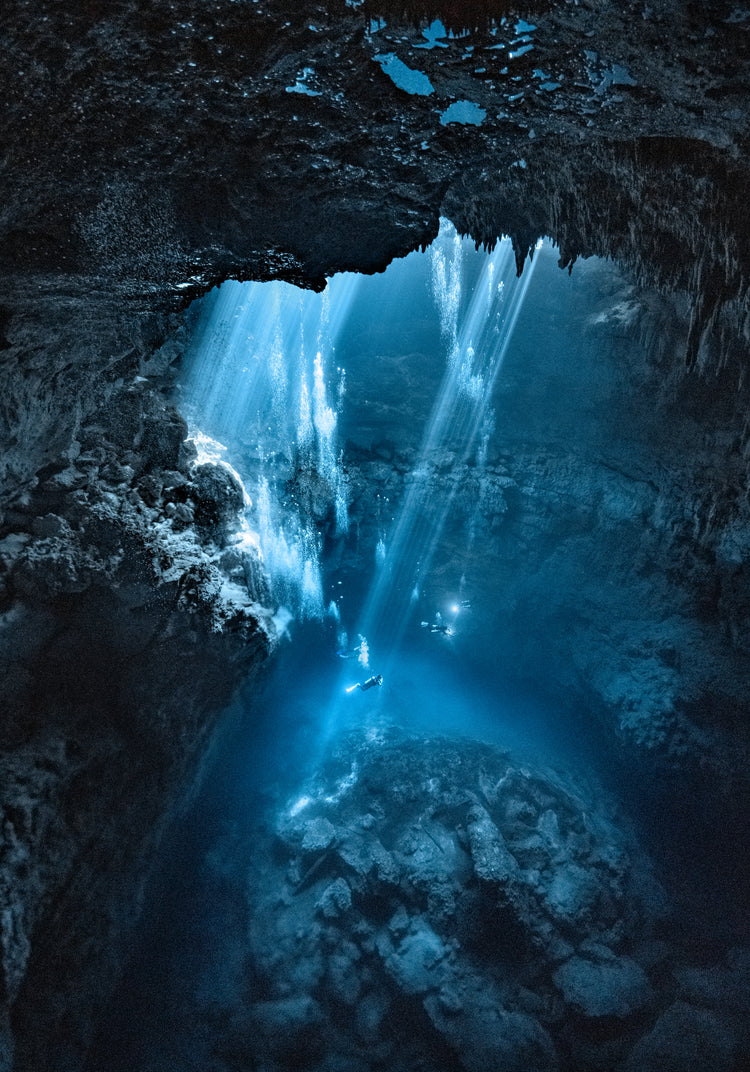 Divers exploring a deep blue water cave.