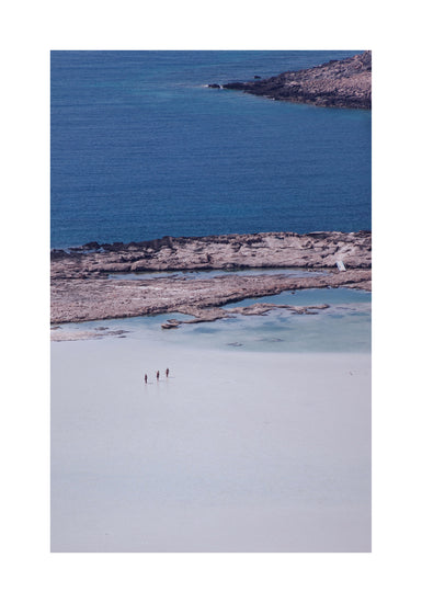 Three people walking in the shallows, heading towards the deep blue ocean ahead.