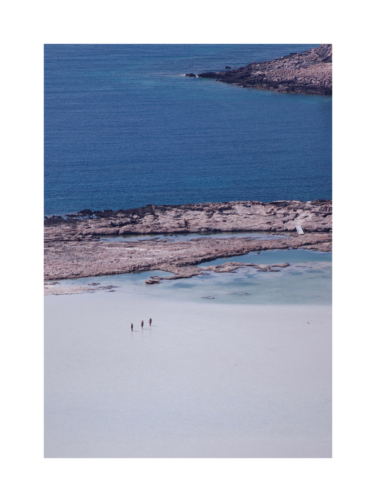 Three people walking in the shallows, heading towards the deep blue ocean ahead.