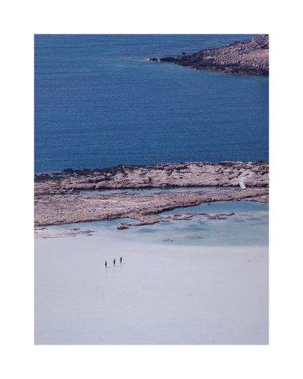 Three people walking in the shallows, heading towards the deep blue ocean ahead.