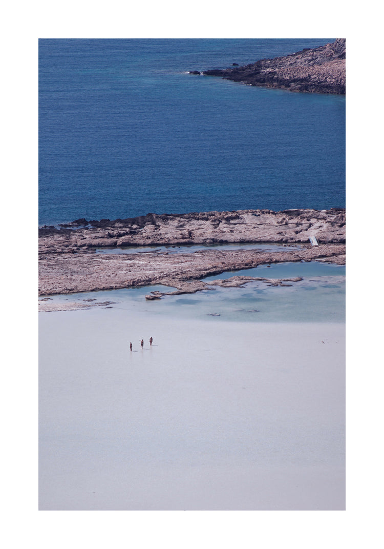 Three people walking in the shallows, heading towards the deep blue ocean ahead.