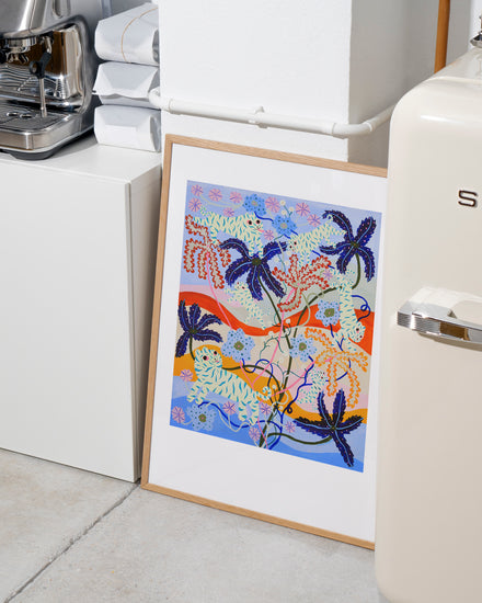 The Mumble Fizz Poster, featuring a colorful abstract design with vibrant blue, orange, pink, and green plants and swirls reminiscent of a playful tiger landscape, leans against a white kitchen cabinet. Nearby sits a cream-colored appliance and neatly stacked towels.