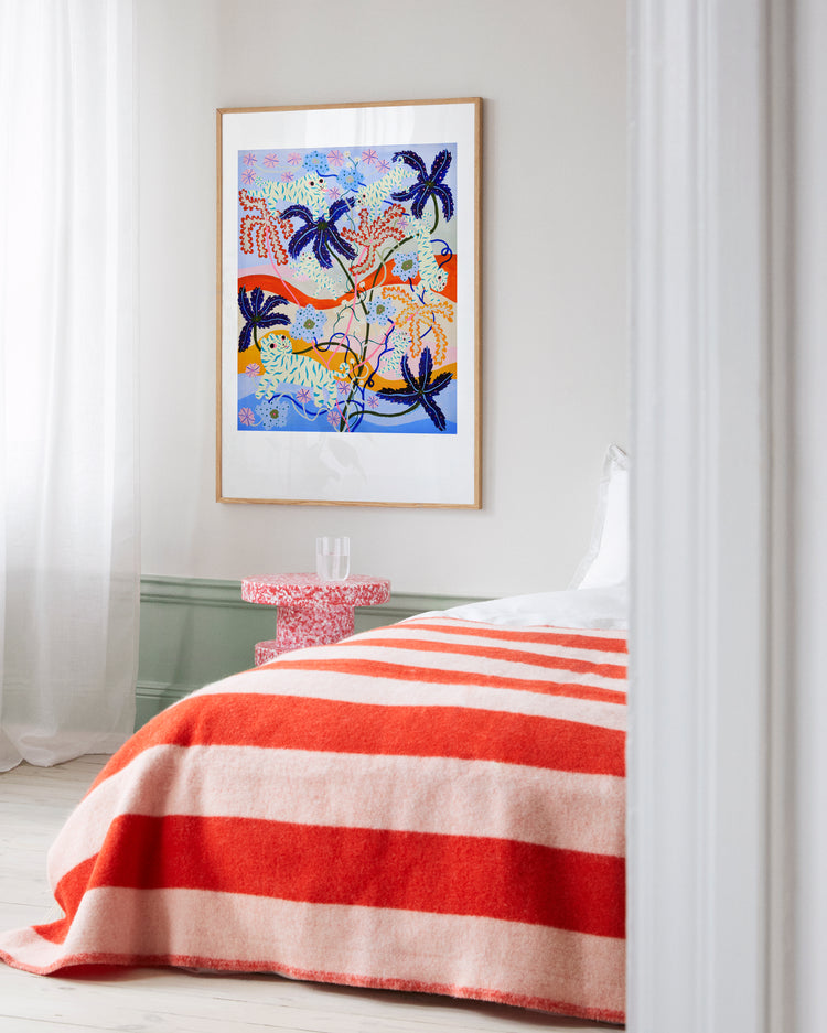 A cozy bedroom features a bed draped with a red and white striped blanket. Above the bed, the Mumble Fizz Poster by Yoyo Nasty showcases abstract patterns and palm trees. The room is softly lit, with sheer white curtains gently fluttering by the window.