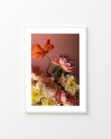 The Sprung Poster presents a framed still life photo on a white wall, featuring a floral arrangement with pink peonies, orange, and yellow flowers against a soft pink background. It emphasizes the vibrant colors and delicate petals of the blossoms.