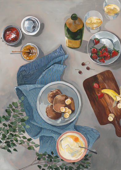 Aerial view of the Breakfast of Champions Poster setup featuring fluffy pancakes with bananas, syrup, and yogurt on a table. A wooden board holds strawberries and cherries. Drinks, a blue-striped cloth, and a leafy branch add to the scenes fresh, inviting atmosphere.
