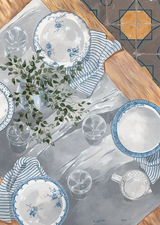 A tabletop scene featuring The Good Plates Poster with blue and white patterns, striped napkins, clear glasses, a jug on wood. A leafy green plant sits on a gray tablecloth above tiled flooring designed by Cat Gerke.