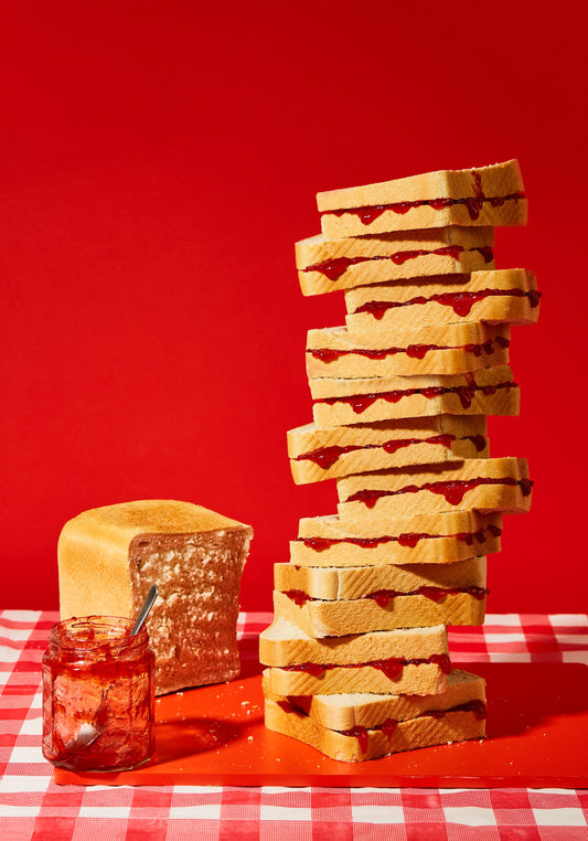 A tower of sandwiches and an empty jam jar on a red and white picnic cloth against a vibrant red backdrop