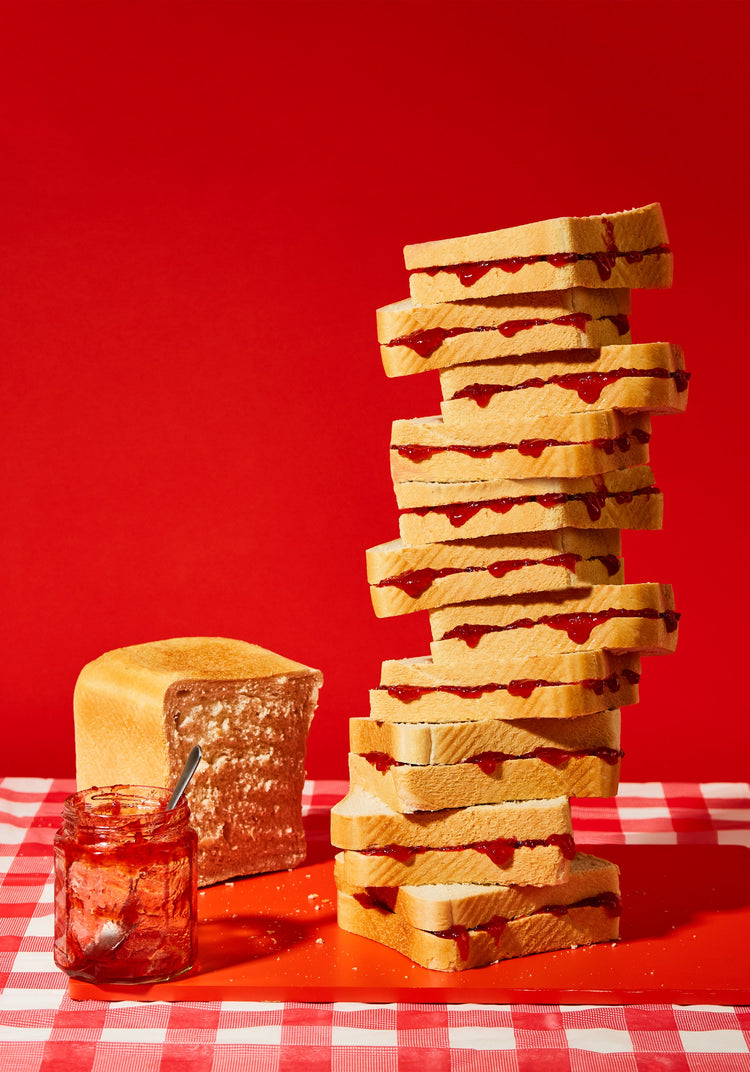 A tower of sandwiches and an empty jam jar on a red and white picnic cloth against a vibrant red backdrop