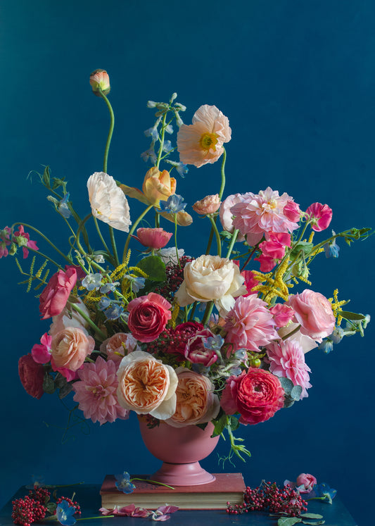 The Pink Kiss Poster showcases a vibrant bouquet of pink, peach, and white flowers, including roses and poppies. Elegantly arranged in a pink vase against a blue background, it features delicate greenery and red berries for a romantic touch.