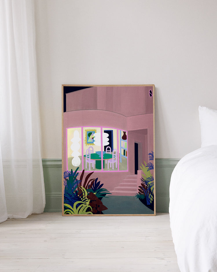 The Lighted Windows 01 Poster, featuring a modern pink building with large windows and surrounding plants, leans against a wall in a room with light-colored walls, a white bed, and sheer curtains.