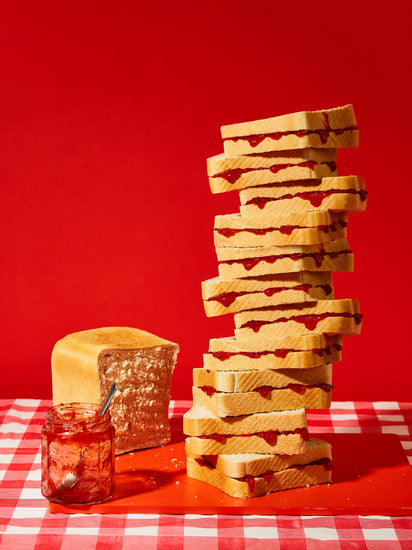 A tower of sandwiches and an empty jam jar on a red and white picnic cloth against a vibrant red backdrop
