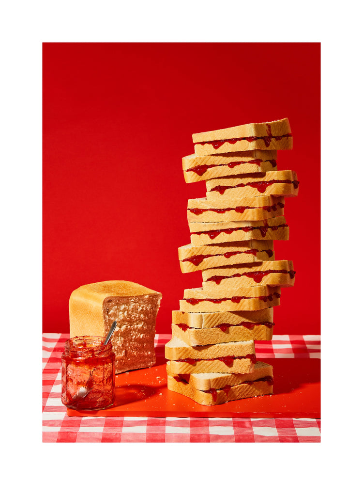 A tower of sandwiches and an empty jam jar on a red and white picnic cloth against a vibrant red backdrop
