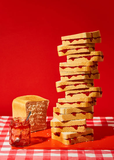 A tower of sandwiches and an empty jam jar on a red and white picnic cloth against a vibrant red backdrop