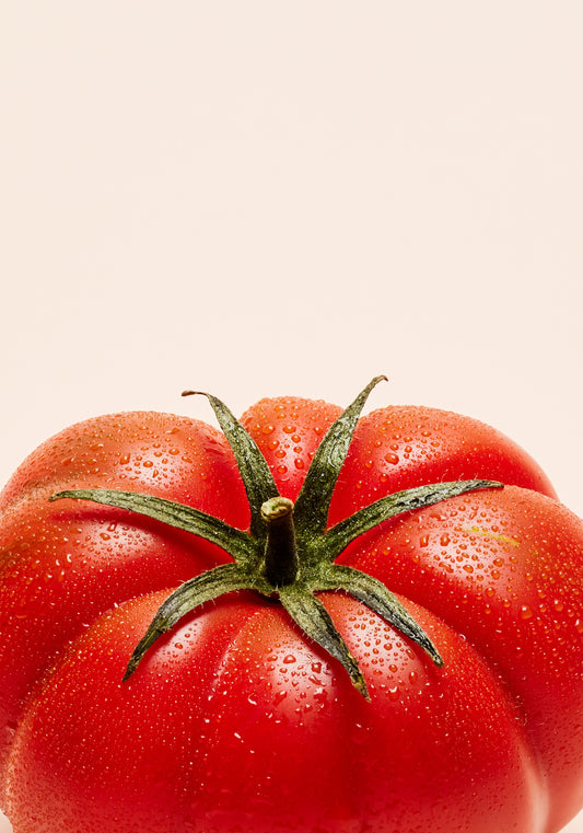 A close-up photograph features a vibrant red tomato adorned with delicate water droplets set against a clean white backdrop.