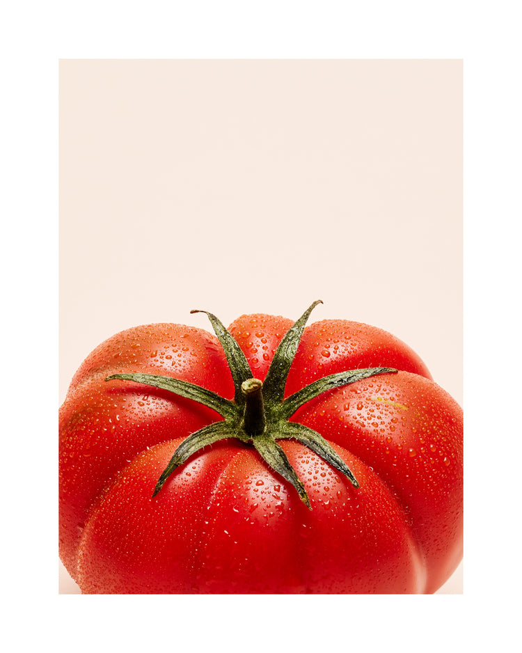 A close-up photograph features a vibrant red tomato adorned with delicate water droplets set against a clean white backdrop. White border.