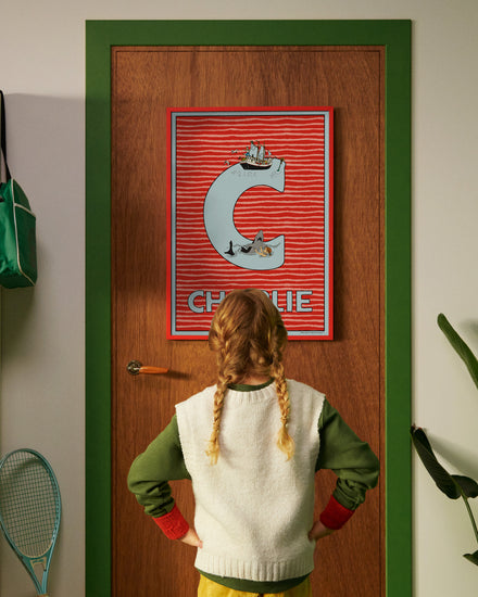 Pippi Longstocking personalised poster featuring the letter C hanging on a door, with a child curiously looking at the artwork.