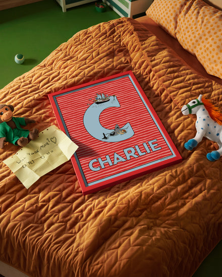 Pippi Longstocking name poster with the letter C and the name Charlie, placed on a neatly made bed in a bright kids’ room.