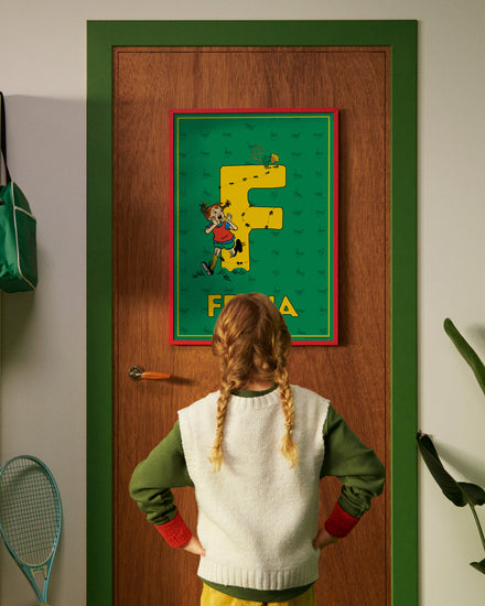 Pippi Longstocking personalised poster featuring the letter F hanging on a door, with a child curiously looking at the artwork.