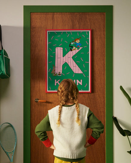 Pippi Longstocking personalised poster featuring the letter K hanging on a door, with a child curiously looking at the artwork.