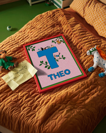 Pippi Longstocking name poster with the letter T and the name Theo, placed on a neatly made bed in a bright kids’ room.