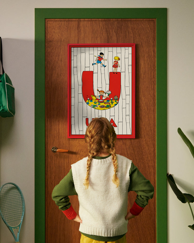Pippi Longstocking personalised poster featuring the letter U hanging on a door, with a child curiously looking at the artwork.
