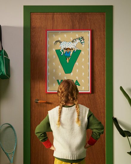 Pippi Longstocking personalised poster featuring the letter V hanging on a door, with a child curiously looking at the artwork.