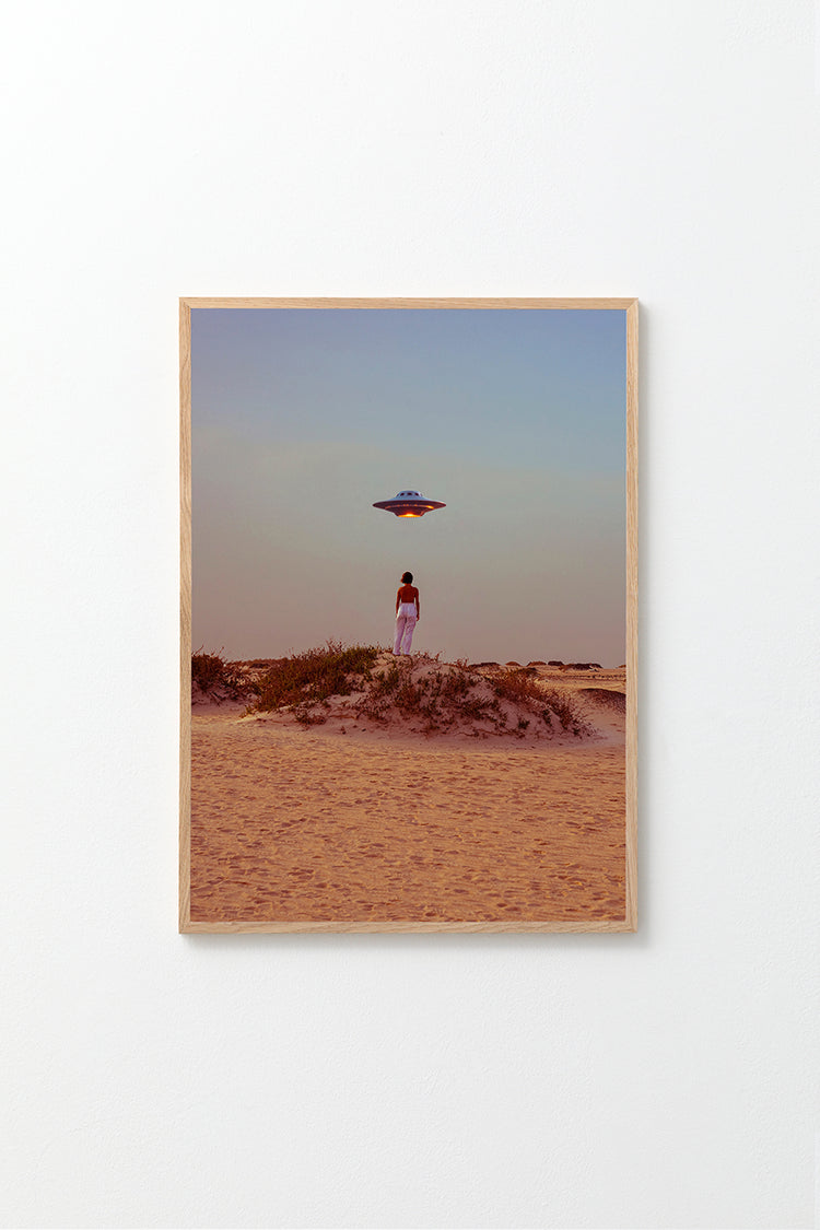 The Hey Luke, our Uber is Here! poster shows a person on a sandy desert dune at sunset, taking a self-portrait while looking at a hovering UFO. Vegetation dots the ground as the sky shifts from blue to orange.