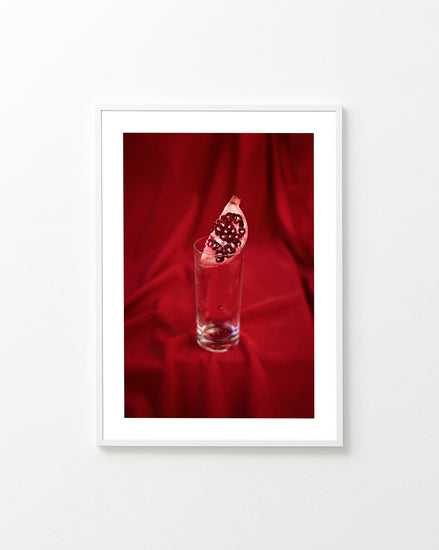 Slice of pomegranate in a glass standing on a blood red sheet.