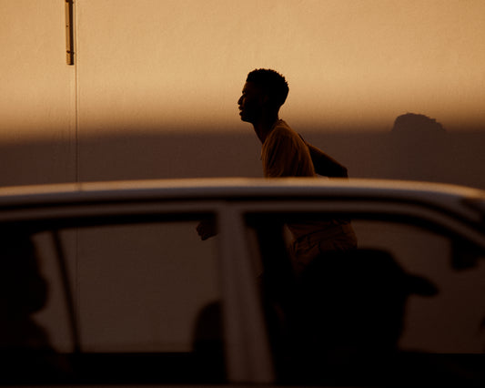 Man dressed in beige running in the opposite direction of a car in front of him.