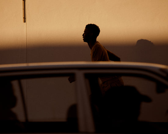 Man dressed in beige running in the opposite direction of a car in front of him.