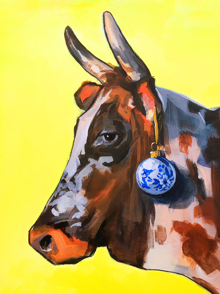 Profile portrait of a bull with a blue Christmas ornament hanging from its ear.