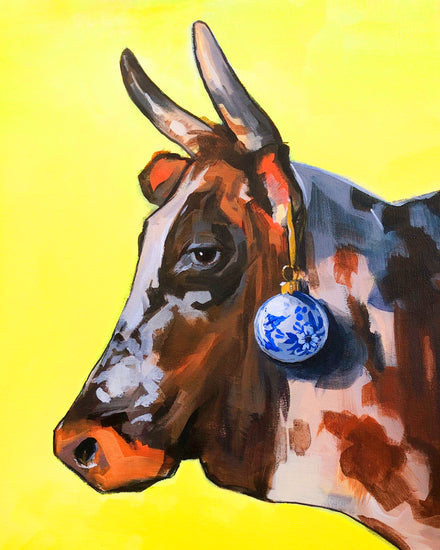 Profile portrait of a bull with a blue Christmas ornament hanging from its ear.