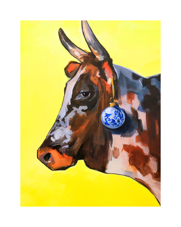 Profile portrait of a bull with a blue Christmas ornament hanging from its ear.